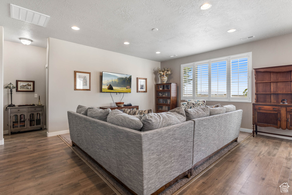 Living room with wood-type flooring, a textured ceiling, recessed lighting, and baseboards