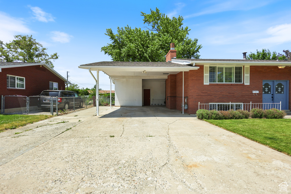 View of front facade with driveway, a carport, brick siding, and a chimney