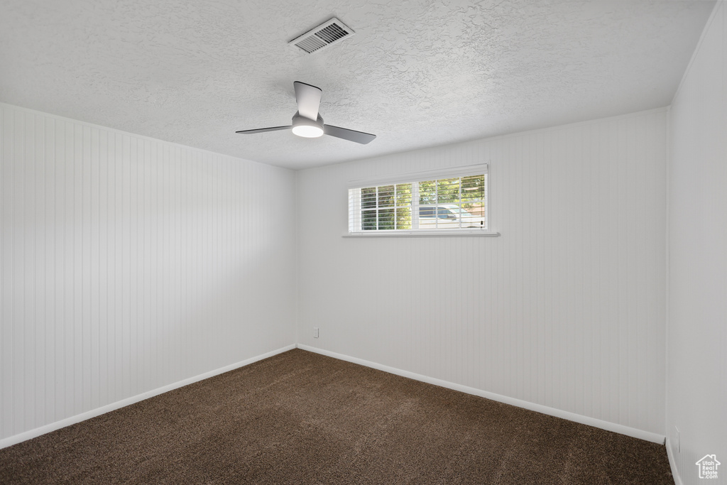 Empty room featuring dark colored carpet, ceiling fan, and a textured ceiling