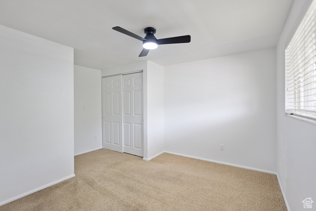 Unfurnished bedroom featuring light colored carpet, a closet, baseboards, and ceiling fan