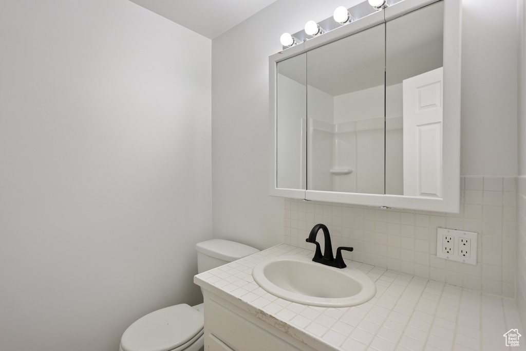 Bathroom featuring toilet, vanity, and decorative backsplash