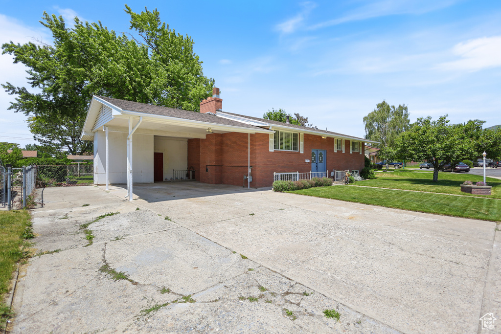 View of front of property with concrete driveway, a carport, a chimney, and brick siding