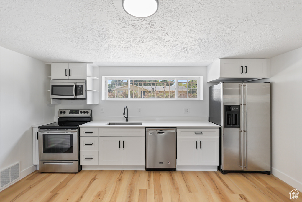 Kitchen with appliances with stainless steel finishes, a sink, open shelves, light wood finished floors, and a textured ceiling