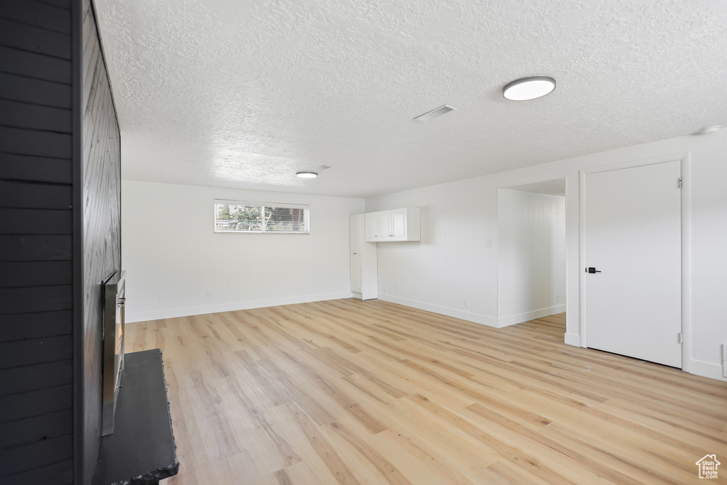 Unfurnished living room featuring a textured ceiling, light wood finished floors, and baseboards