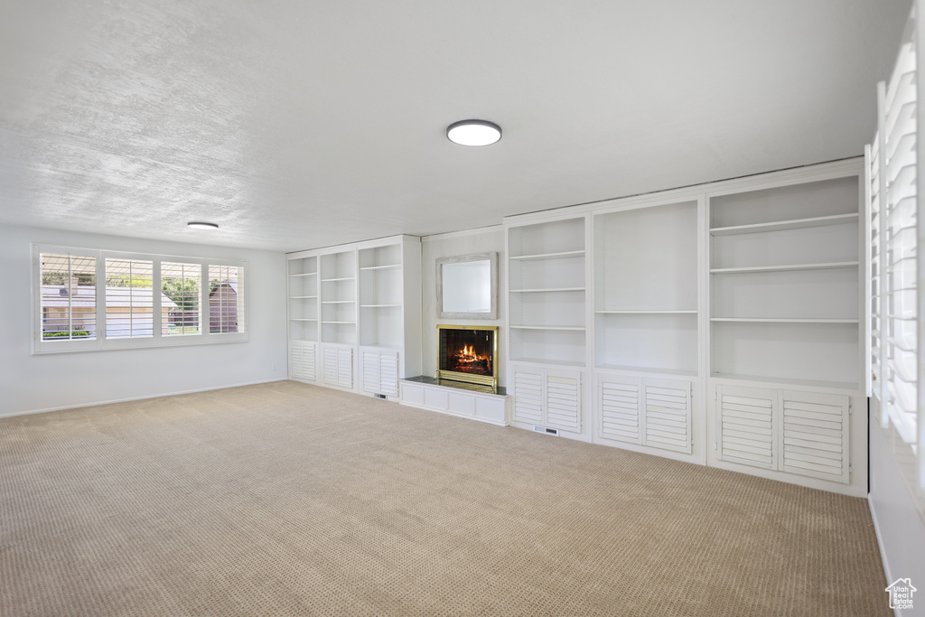 Unfurnished living room featuring carpet floors, a tiled fireplace, and baseboards