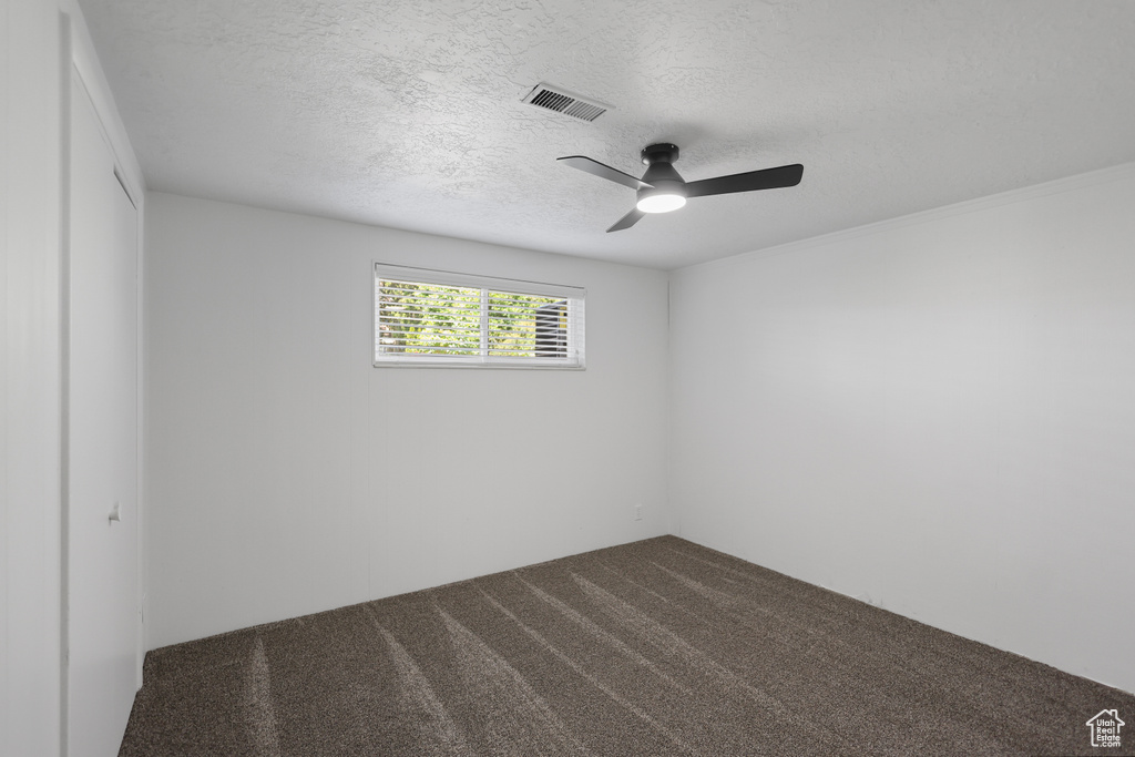Empty room featuring dark carpet, a textured ceiling, and ceiling fan