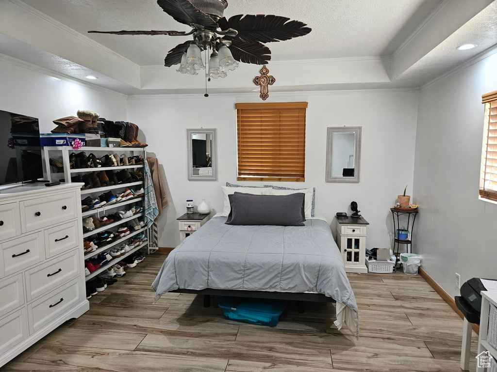 Bedroom with a tray ceiling, ornamental molding, light wood finished floors, baseboards, and recessed lighting