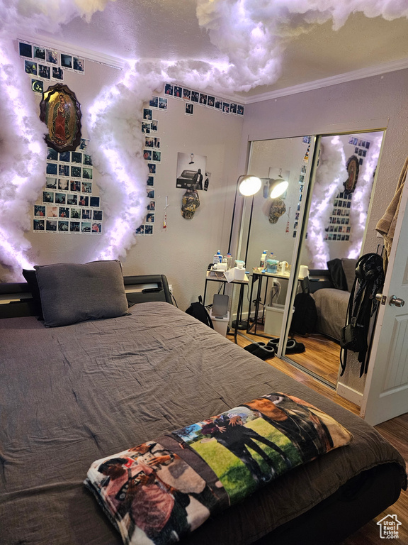 Bedroom with wood finished floors, ornamental molding, and a closet