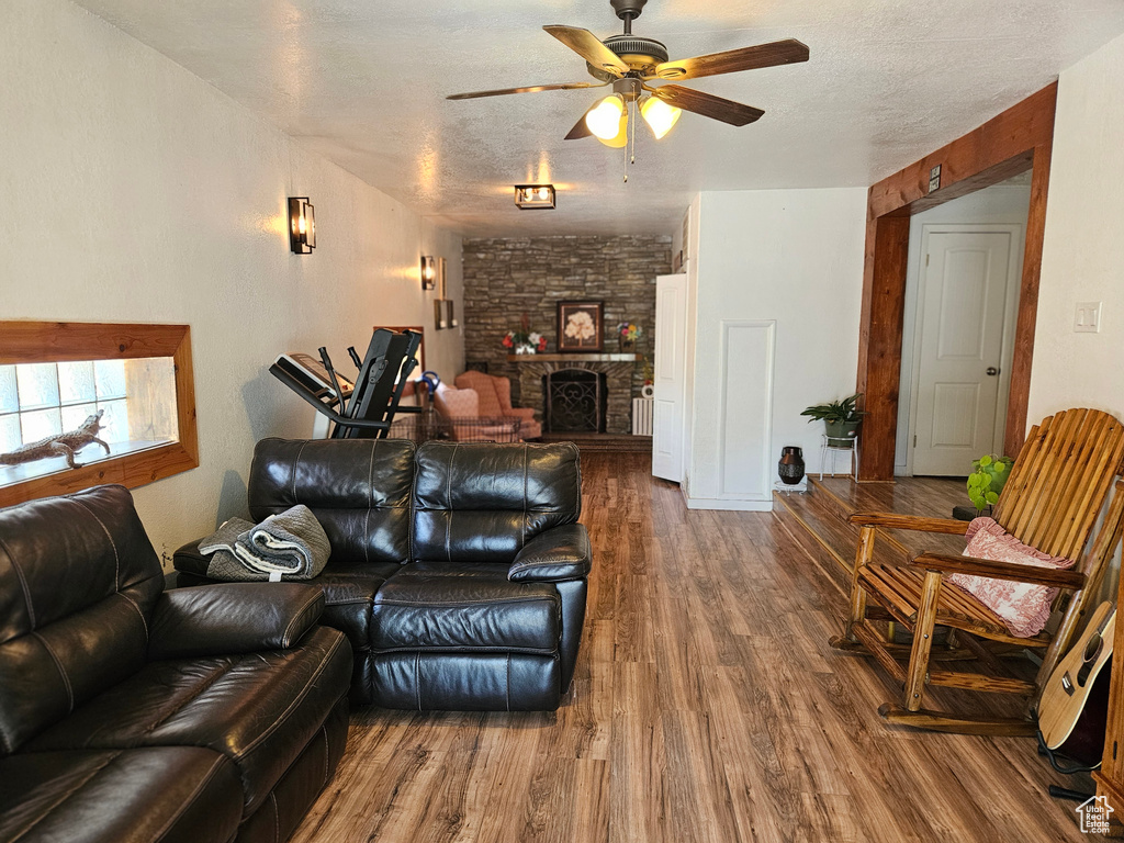 Living area with ceiling fan, wood finished floors, a stone fireplace, and a textured ceiling