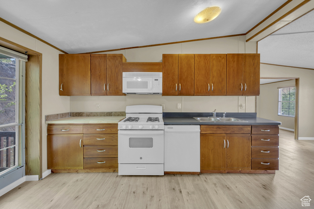 Kitchen featuring white appliances, vaulted ceiling, a sink, light wood-style floors, and ornamental molding
