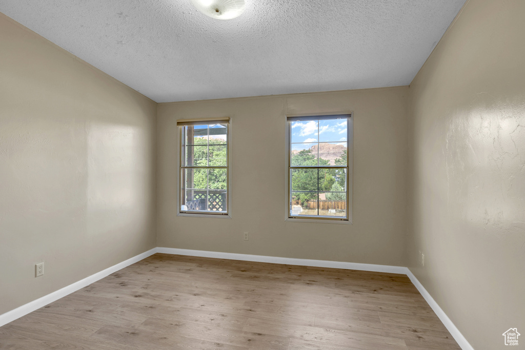 Spare room with a textured ceiling, light wood-type flooring, baseboards, and vaulted ceiling