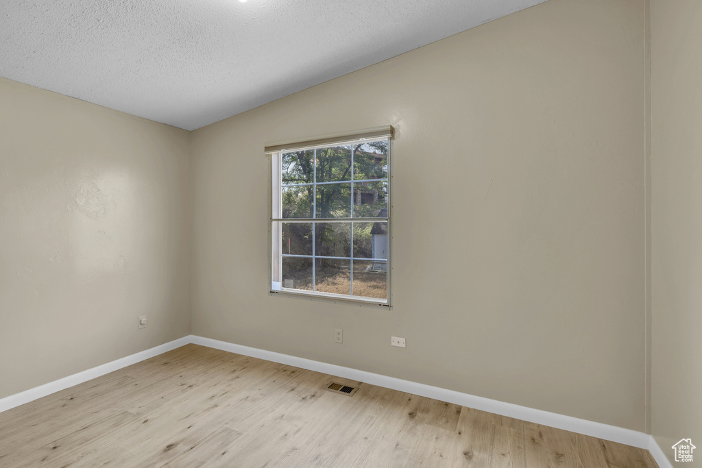 Spare room featuring wood finished floors, baseboards, a textured ceiling, and vaulted ceiling