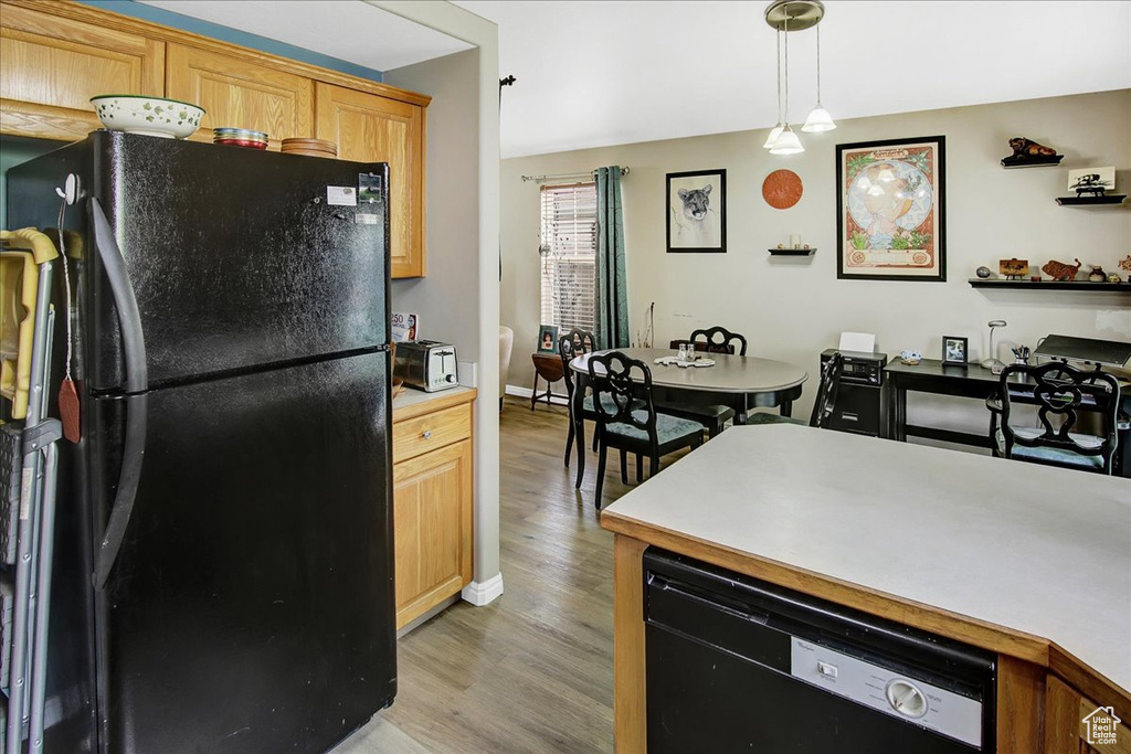 Kitchen featuring black appliances, light wood-style floors, light countertops, hanging light fixtures, and baseboards