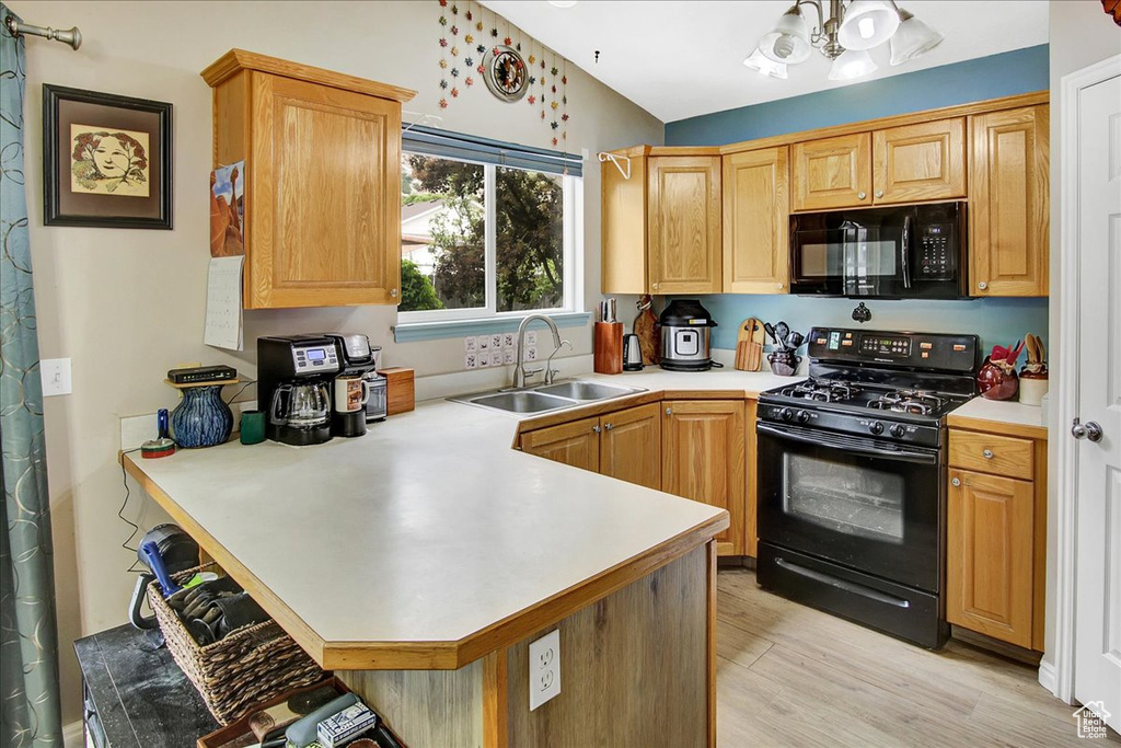 Kitchen featuring black appliances, a sink, a peninsula, light countertops, and light wood-style floors