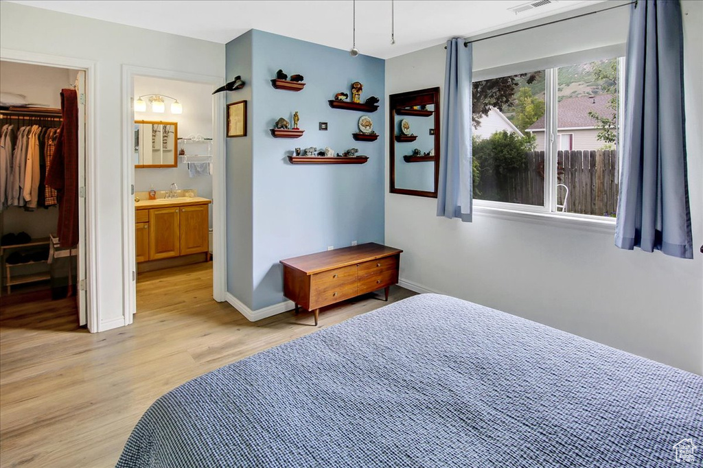 Bedroom featuring light wood finished floors, baseboards, a walk in closet, connected bathroom, and a sink