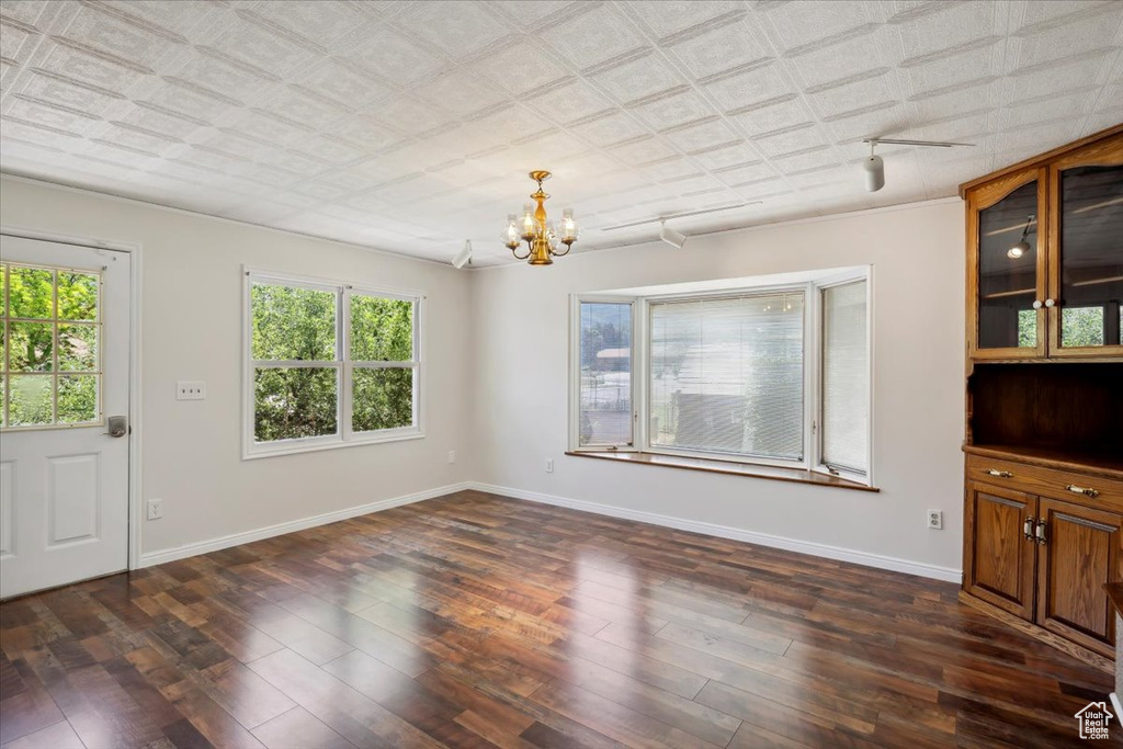 Unfurnished living room with a chandelier, dark wood finished floors, and baseboards