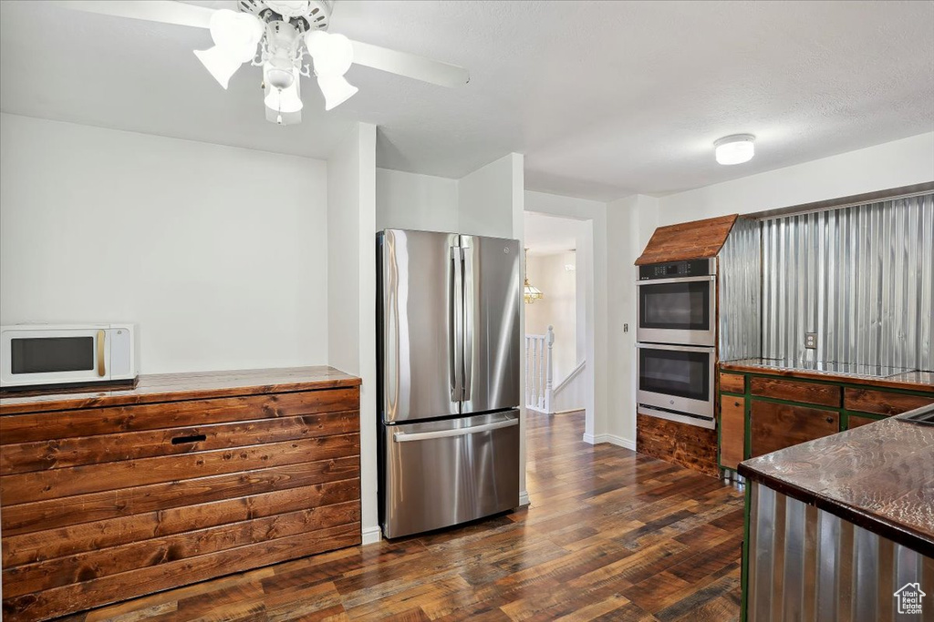 Kitchen featuring appliances with stainless steel finishes, dark countertops, dark wood finished floors, a ceiling fan, and baseboards