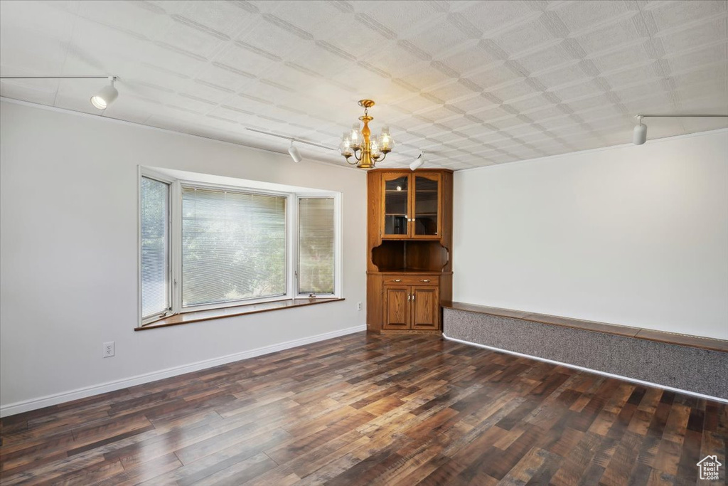 Spare room with track lighting, a chandelier, dark wood-type flooring, and baseboards