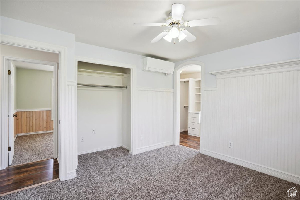 Unfurnished bedroom featuring carpet floors, a closet, a wainscoted wall, arched walkways, and a wall mounted AC