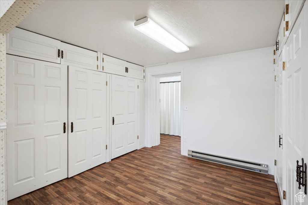 Unfurnished bedroom featuring baseboard heating and dark wood-style floors