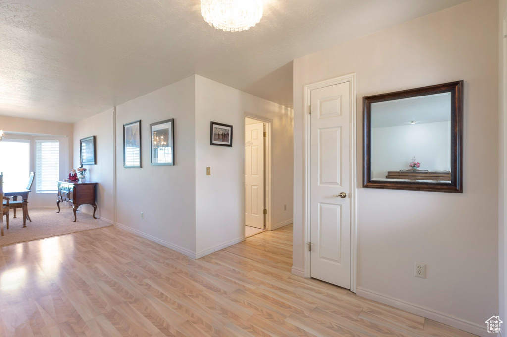 Unfurnished room with a chandelier, light wood-style floors, baseboards, and a textured ceiling