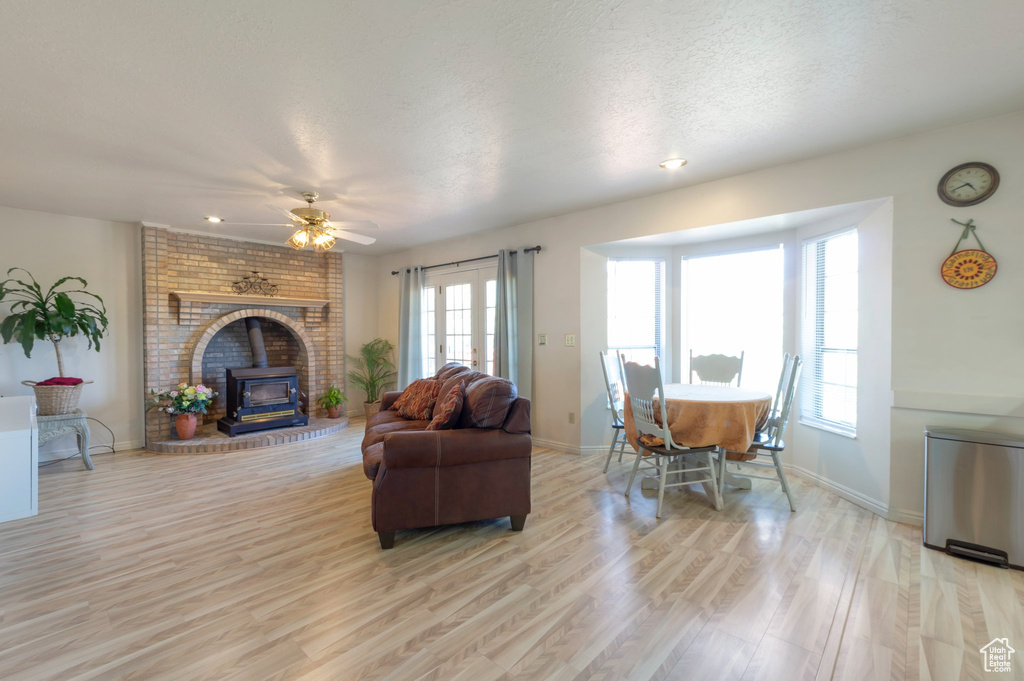 Living area featuring a wood stove, light wood-style floors, baseboards, ceiling fan, and a textured ceiling