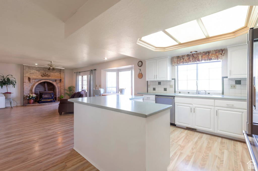 Kitchen with stainless steel dishwasher, a kitchen island, backsplash, open floor plan, and light wood-type flooring