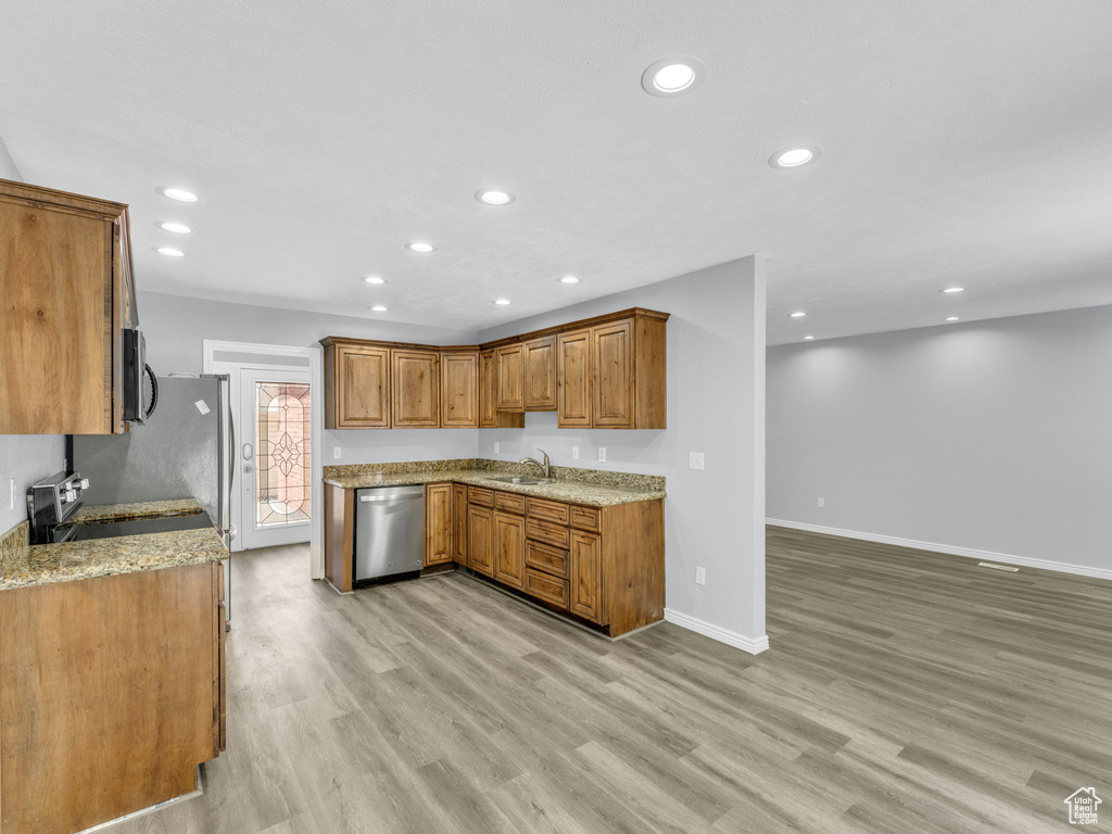 Kitchen featuring appliances with stainless steel finishes, brown cabinetry, light wood-style floors, a sink, and recessed lighting