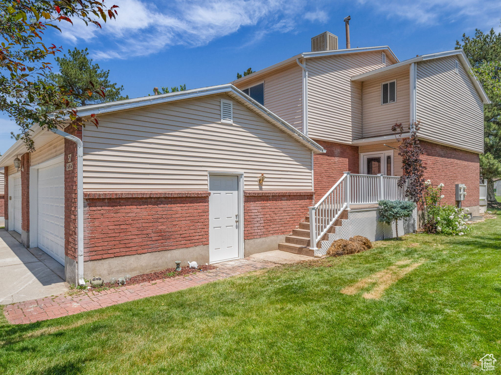 Back of property featuring brick siding, a garage, a lawn, and concrete driveway