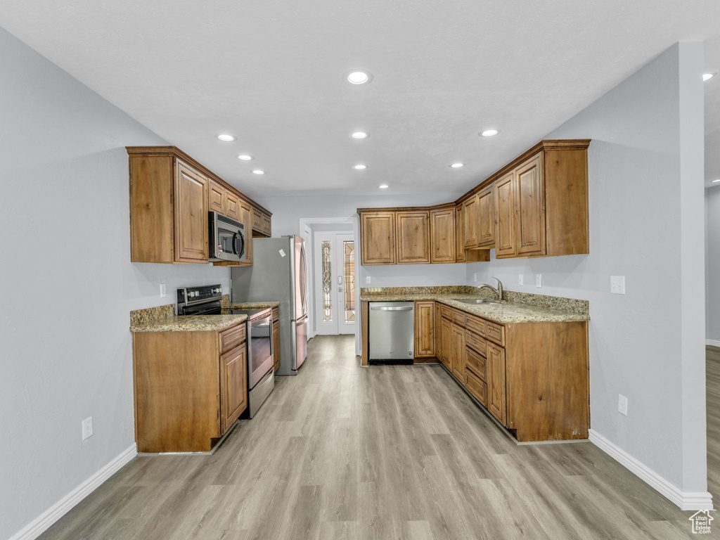 Kitchen with stainless steel appliances, a sink, light wood-type flooring, brown cabinetry, and baseboards