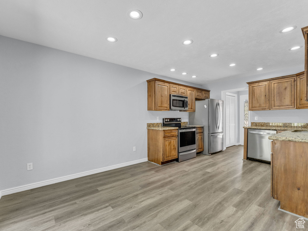 Kitchen featuring appliances with stainless steel finishes, recessed lighting, light wood-type flooring, baseboards, and light stone countertops
