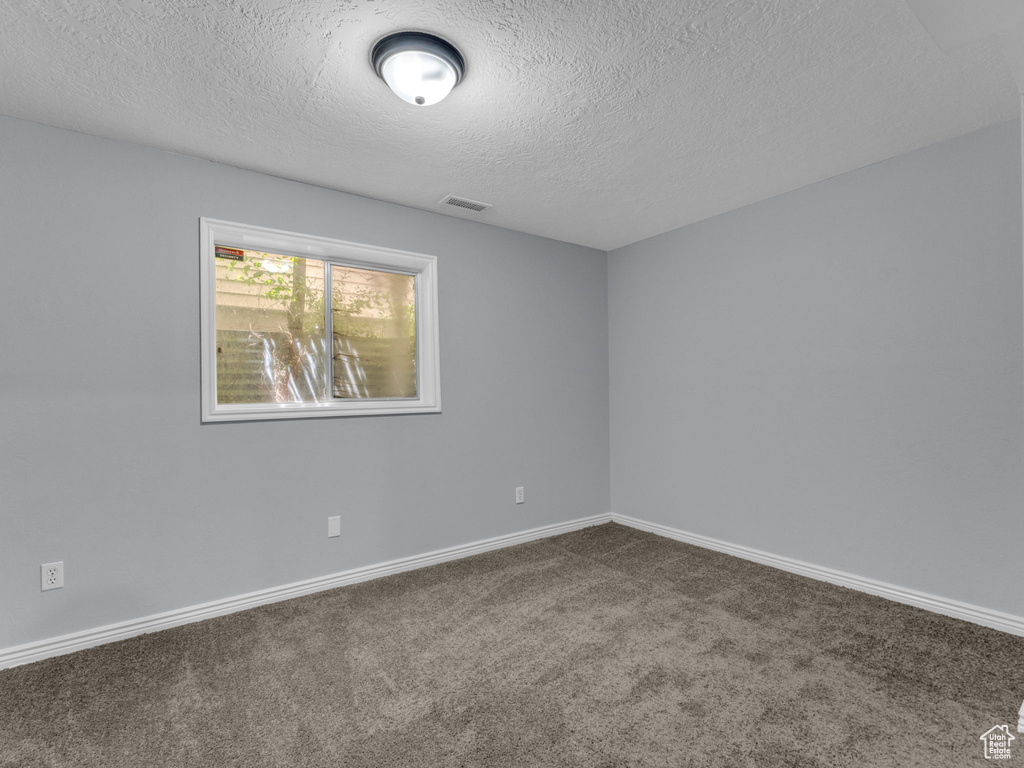 Empty room featuring dark carpet, a textured ceiling, and baseboards