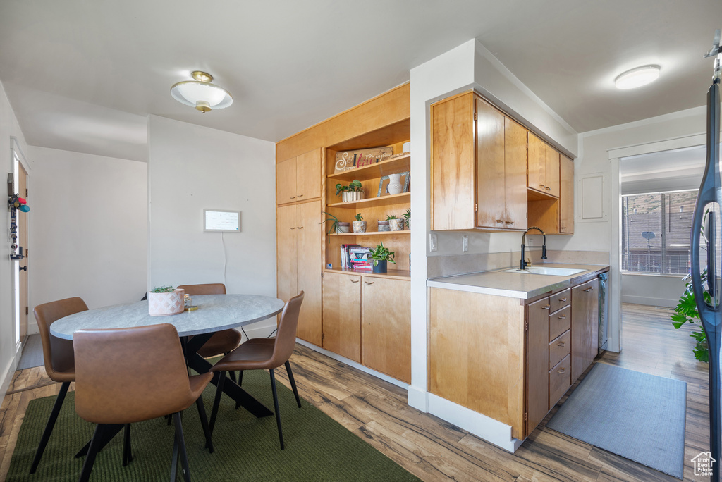 Kitchen with a sink, light wood-type flooring, light countertops, open shelves, and stainless steel fridge