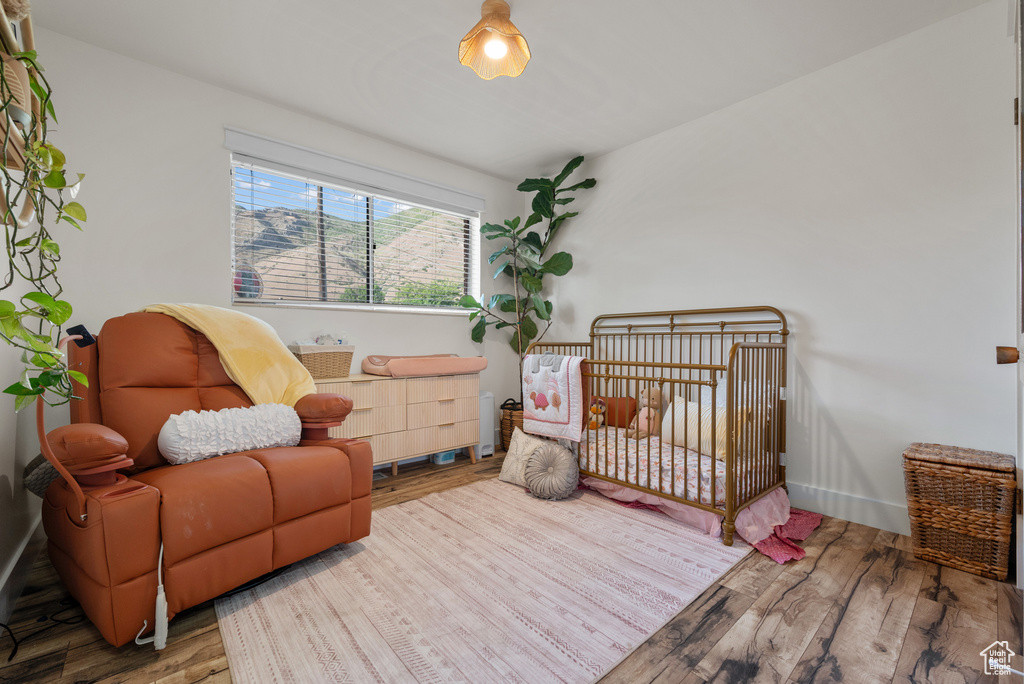 Bedroom featuring wood finished floors, a crib, and baseboards