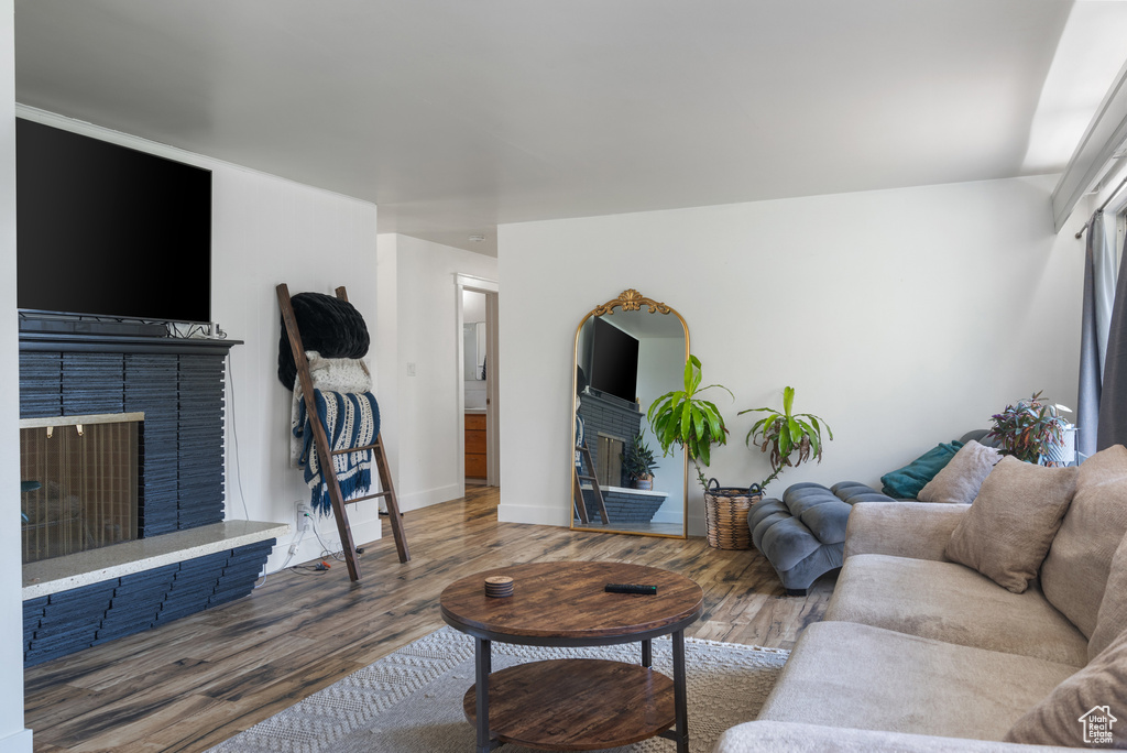 Living room with a brick fireplace, wood finished floors, and baseboards