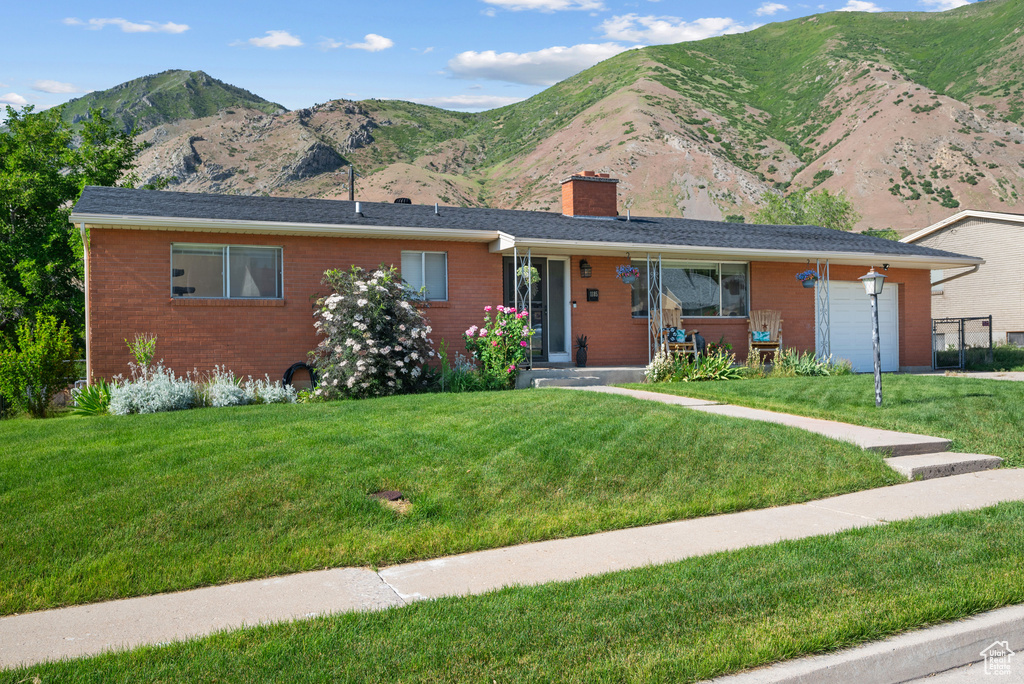 Ranch-style home featuring brick siding, a chimney, an attached garage, and a front yard