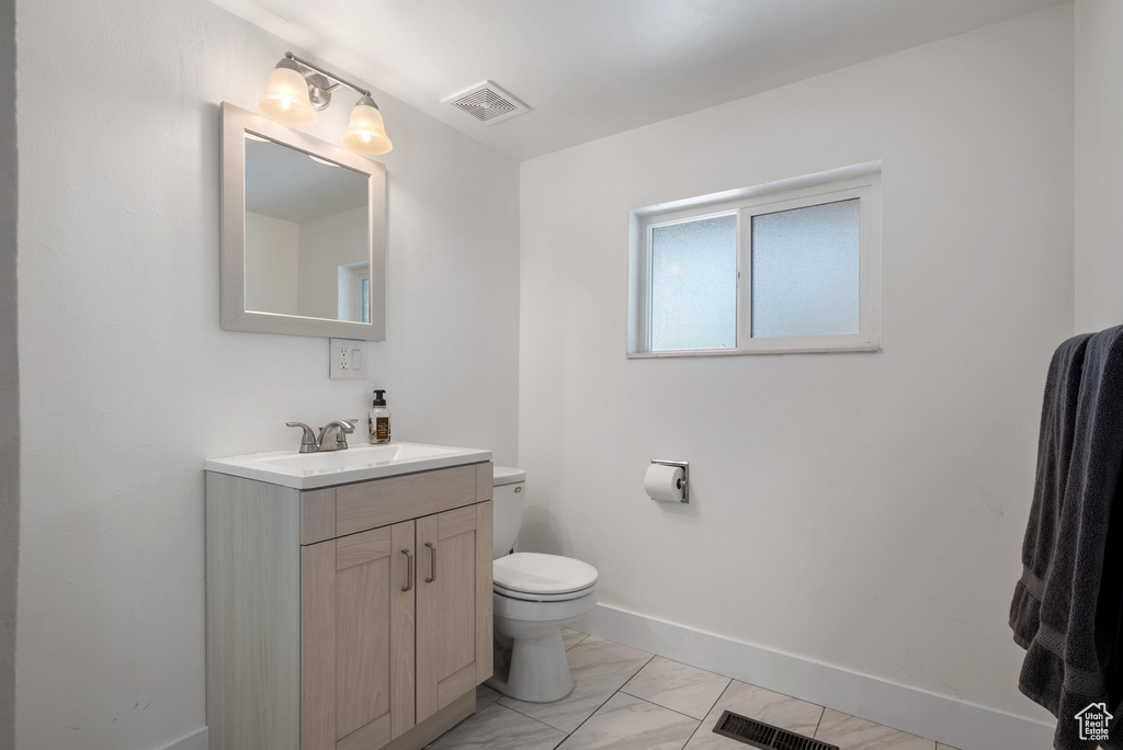 Half bathroom with vanity, toilet, marble look tiles, and baseboards