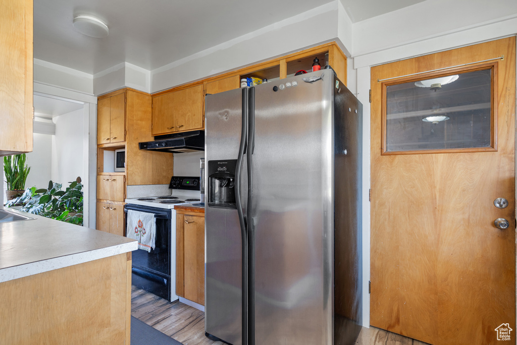 Kitchen with stainless steel fridge with ice dispenser, under cabinet range hood, range with electric cooktop, light countertops, and light wood-type flooring