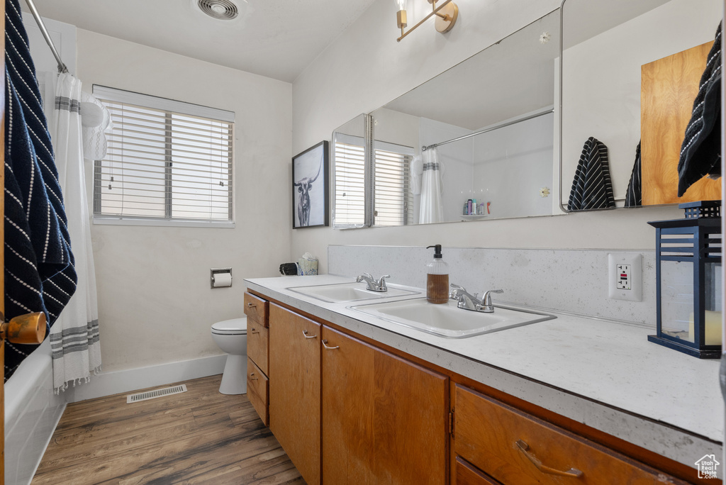 Full bath with double vanity, toilet, wood finished floors, shower / bathtub combination with curtain, and baseboards