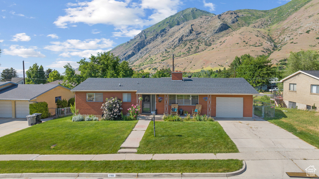 Ranch-style home featuring concrete driveway, a mountain view, a chimney, brick siding, and an attached garage