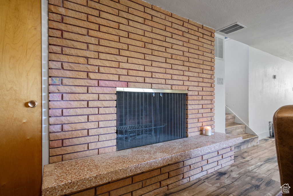 Detailed view of a brick fireplace, wood finished floors, and a textured ceiling