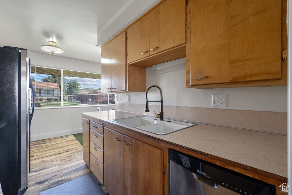Kitchen with appliances with stainless steel finishes, a sink, light wood-style floors, light countertops, and baseboards
