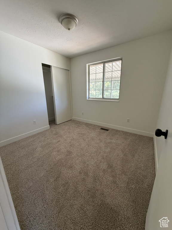 Unfurnished bedroom with baseboards, a closet, a textured ceiling, and light carpet