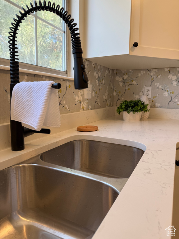 Kitchen view of a sink, white cabinets, and light stone countertops
