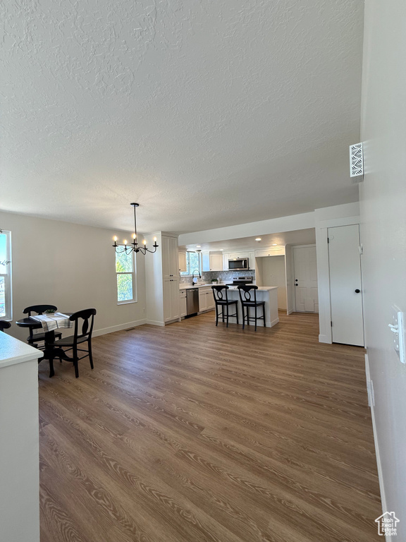 Living area with dark wood-type flooring, a textured ceiling, baseboards, and a chandelier