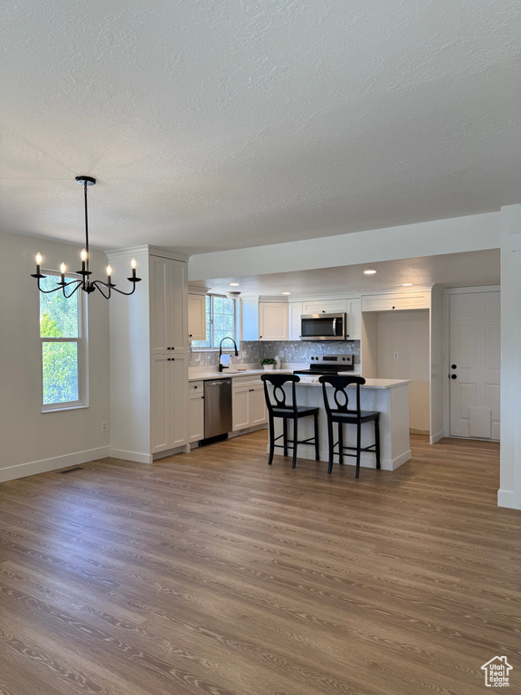 Kitchen featuring stainless steel appliances, baseboards, wood finished floors, a chandelier, and a textured ceiling