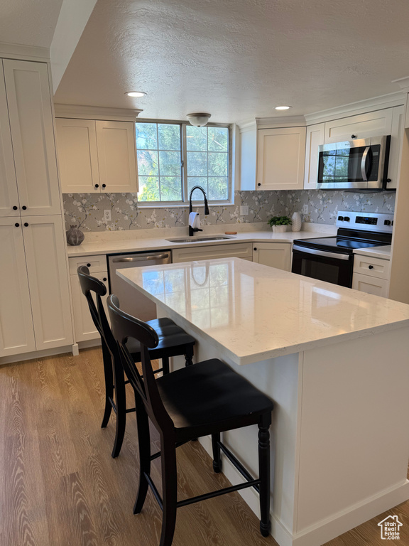 Kitchen with stainless steel appliances, a sink, white cabinetry, light wood-style flooring, and a textured ceiling
