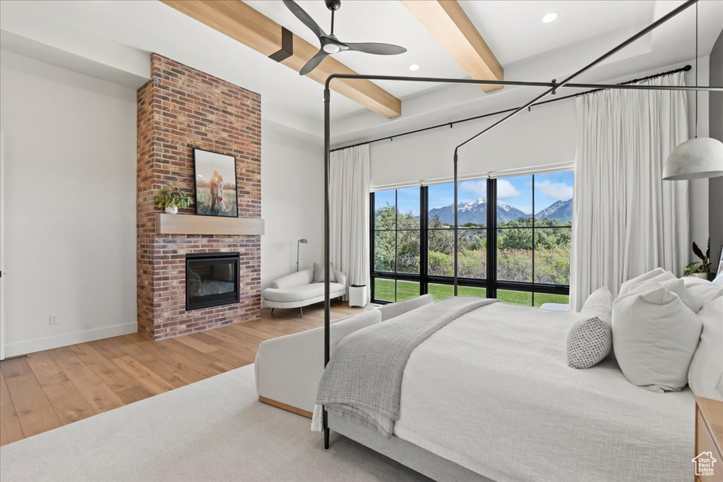 Bedroom featuring beam ceiling, wood finished floors, a fireplace, a mountain view, and baseboards