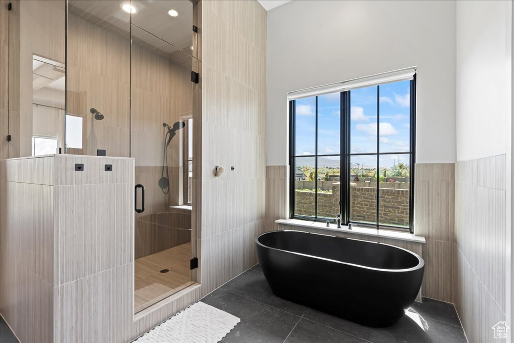 Full bath with tile walls, a freestanding tub, a shower stall, a towering ceiling, and tile patterned flooring