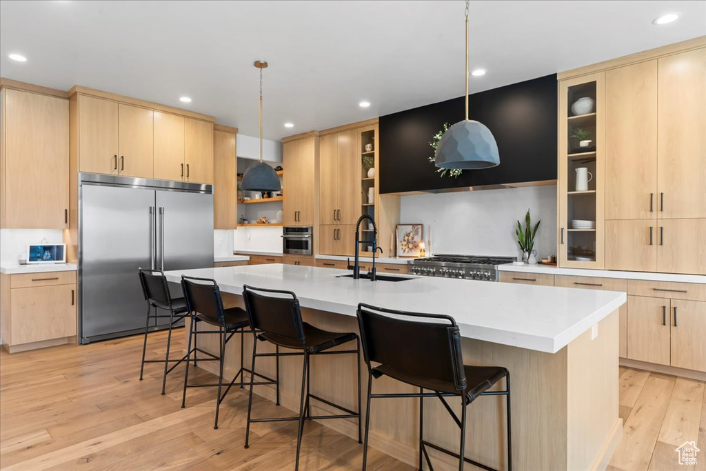 Kitchen featuring appliances with stainless steel finishes, light brown cabinetry, light wood finished floors, an island with sink, and a sink